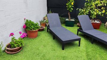 Un patio con due poltrone nere, erba sintetica verde e piante in vaso.