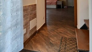 Un couloir doté d’un plancher en bois, d’un rideau à motifs et d’une porte donnant sur une chambre à coucher, où se trouvent un lit et une table de chevet.