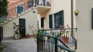 Une cour étroite avec un escalier menant à un balcon, des plantes en pot et un petit ventilateur au rez-de-chaussée.