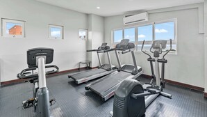 Ein Fitnessraum mit Laufbändern, Crosstrainern und einem Ergometer. Fenster mit Blick, sowie eine Klimaanlage an der Wand.