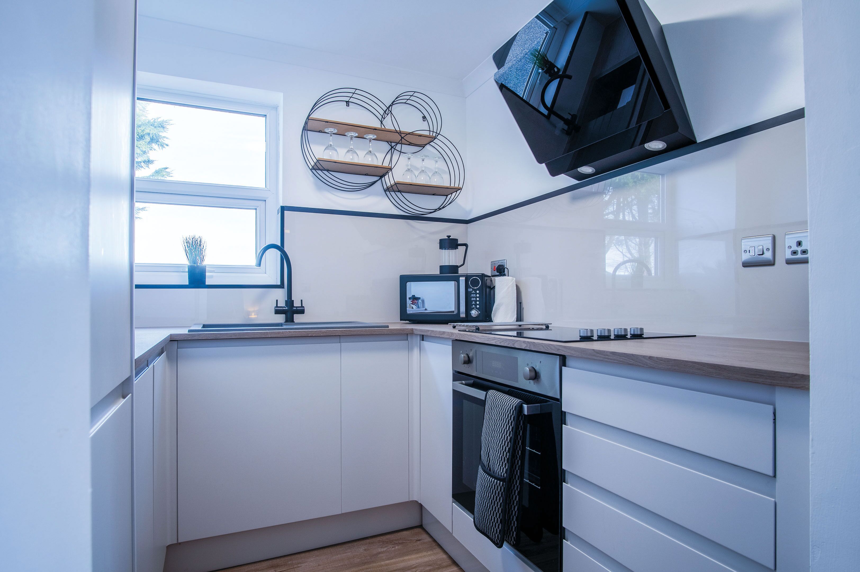 A modern kitchen with white cabinets, a microwave, an oven, and a window with a view of trees.