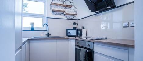 A modern kitchen with white cabinets, a microwave, an oven, and a window with a view of trees.