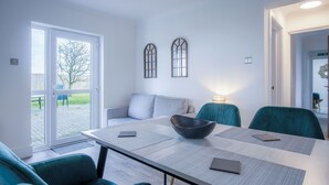 A modern dining area with a long table, teal chairs, and a bowl centerpiece. - Gower Hideaway - 3 Bed - Ocean Breeze (Swansea)