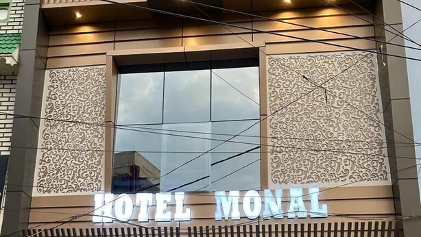 A hotel named "HOTEL MONAL" with a modern facade, large windows, and a visible dining area with tables and chairs.