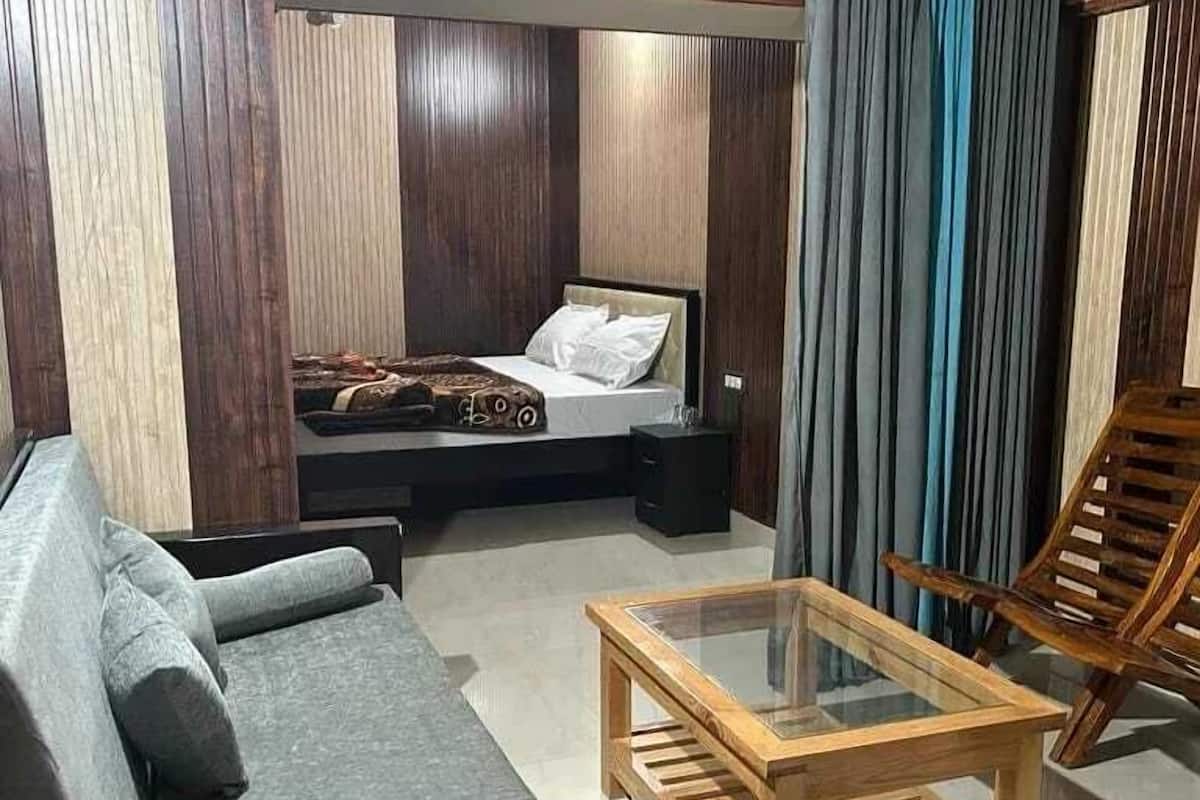 A modern bedroom with a bed, a sofa, a glass-top coffee table, and a wooden chair.