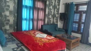 A hotel room with a bed, a sofa, a TV, and a window with curtains.