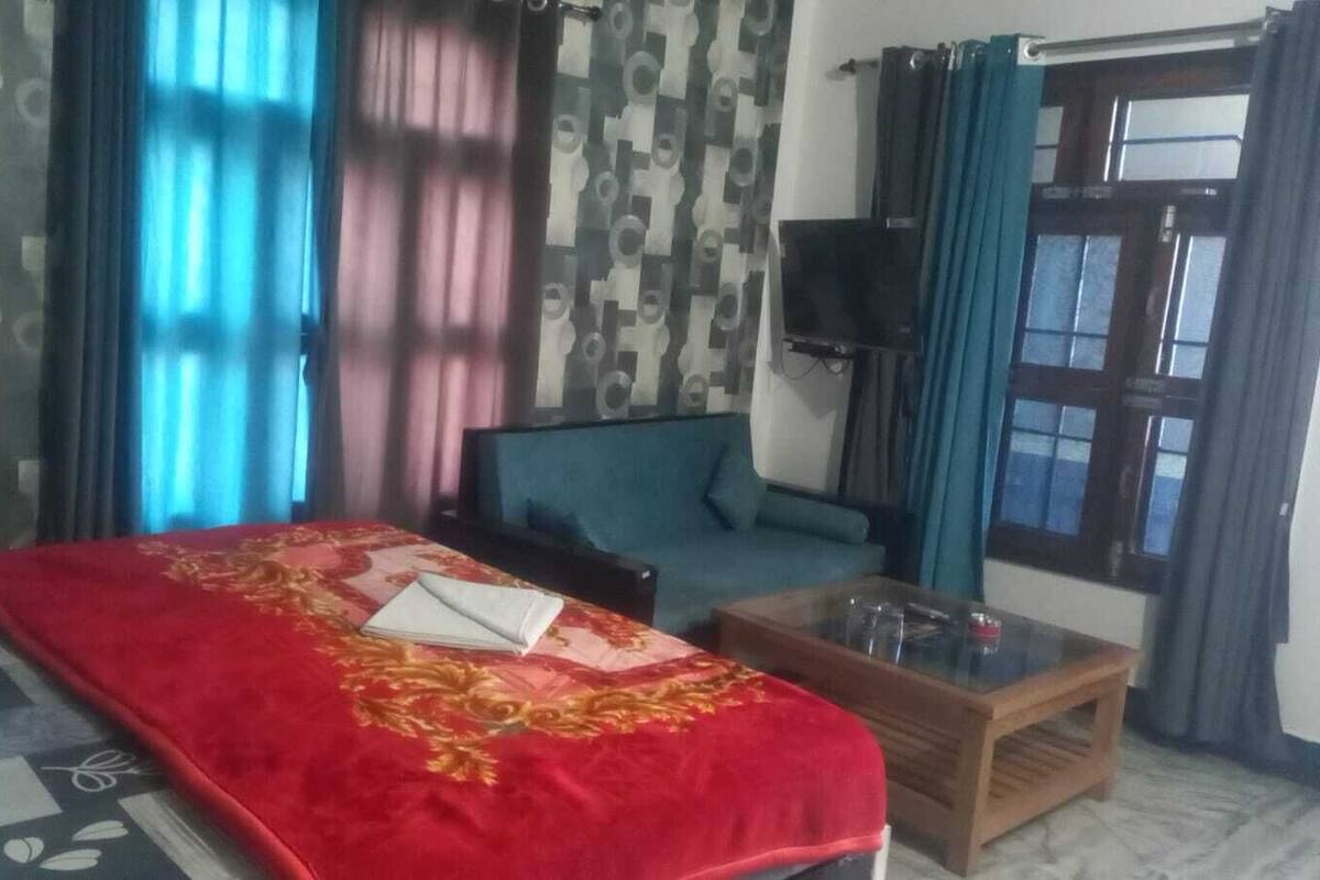 A hotel room with a bed, a sofa, a TV, and a window with curtains.