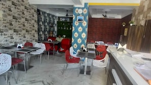 A restaurant with a patterned wall, red and white chairs, and a counter with papers.