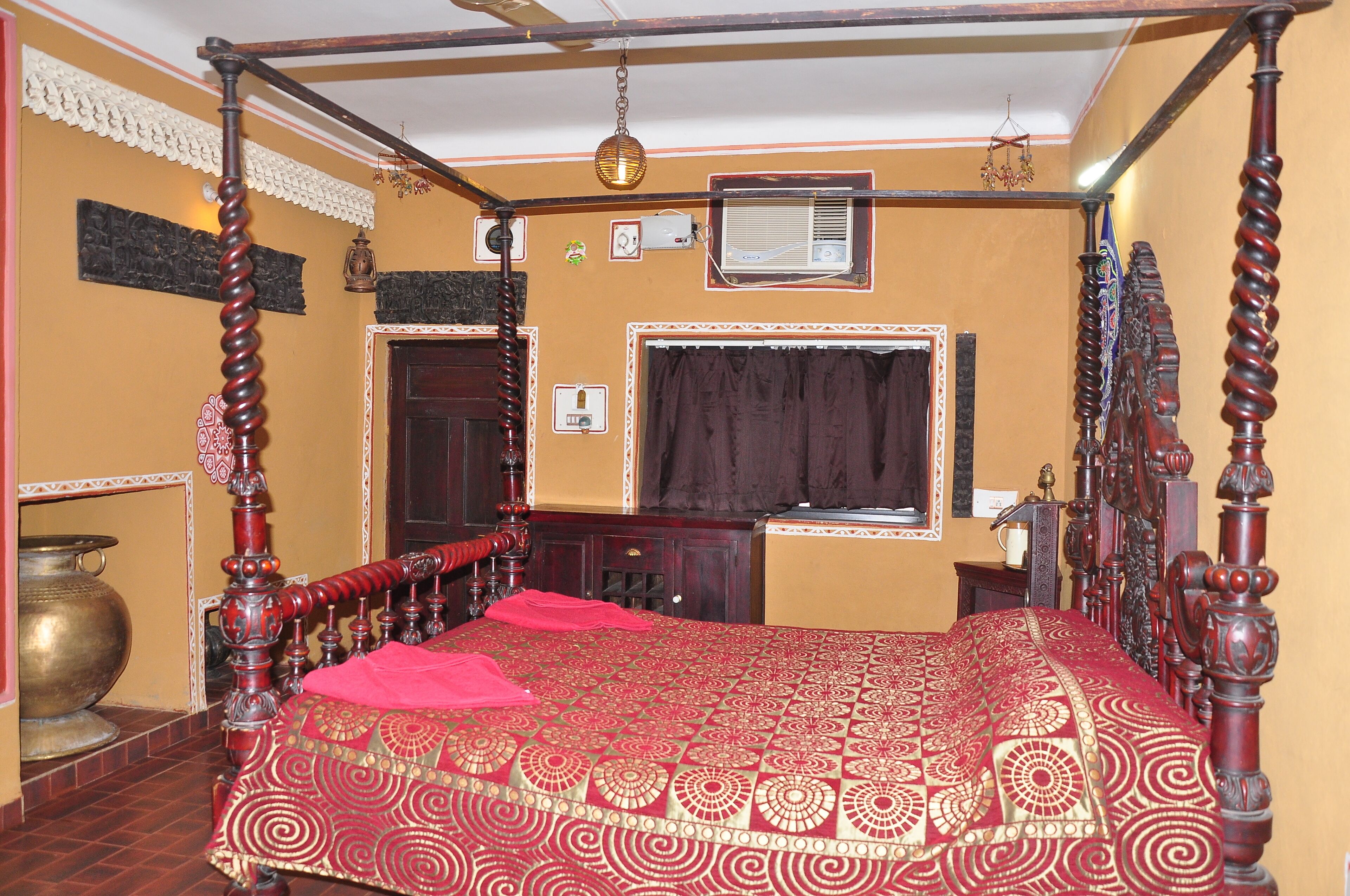 A traditional room with a four-poster bed, a large brass pot, and a window with curtains.