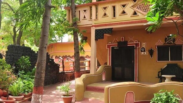A traditional building with a central door, steps leading to the entrance, and potted plants around the area. - NAKHRALI DHANI VILLAGE RESOTR LLP (Indore)