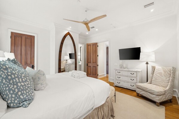 A bedroom with a large bed, a ceiling fan, a TV, a chair, and a dresser.