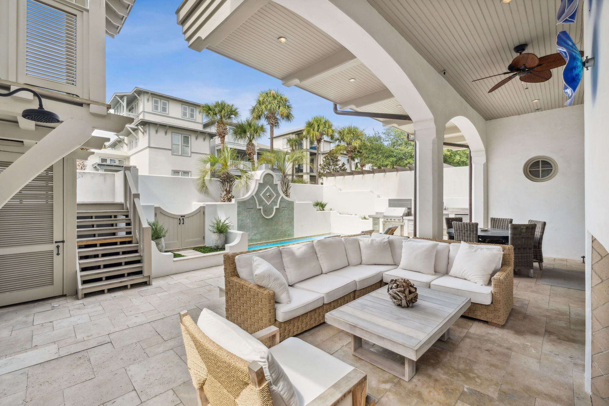 A covered outdoor living area with a sectional sofa, wicker chairs, a coffee table, and a pool.