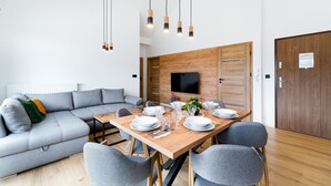 A modern living room with a grey sectional sofa, a wooden dining table set with plates and glasses, and a flat-screen TV mounted on a wooden wall. - Apartamenty Sun & Snow Hillside (Karpacz)