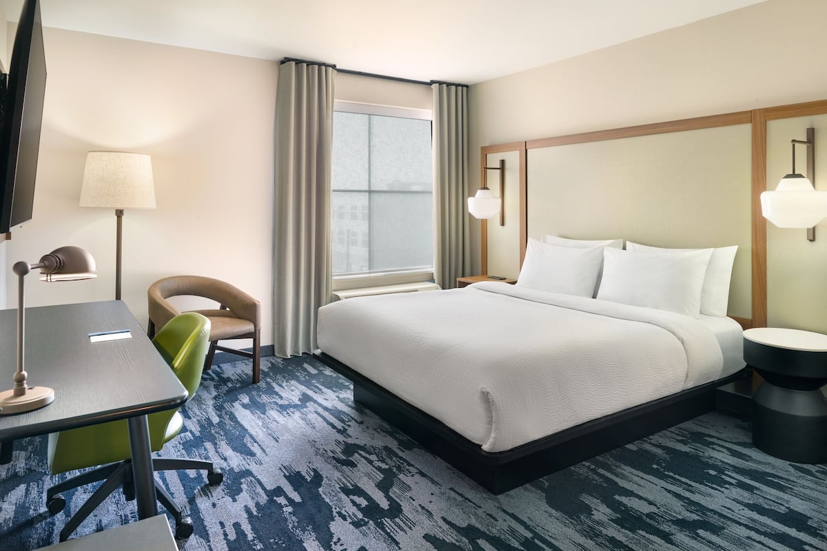 A hotel room with a bed, a desk, a chair, a TV, and a window with curtains.