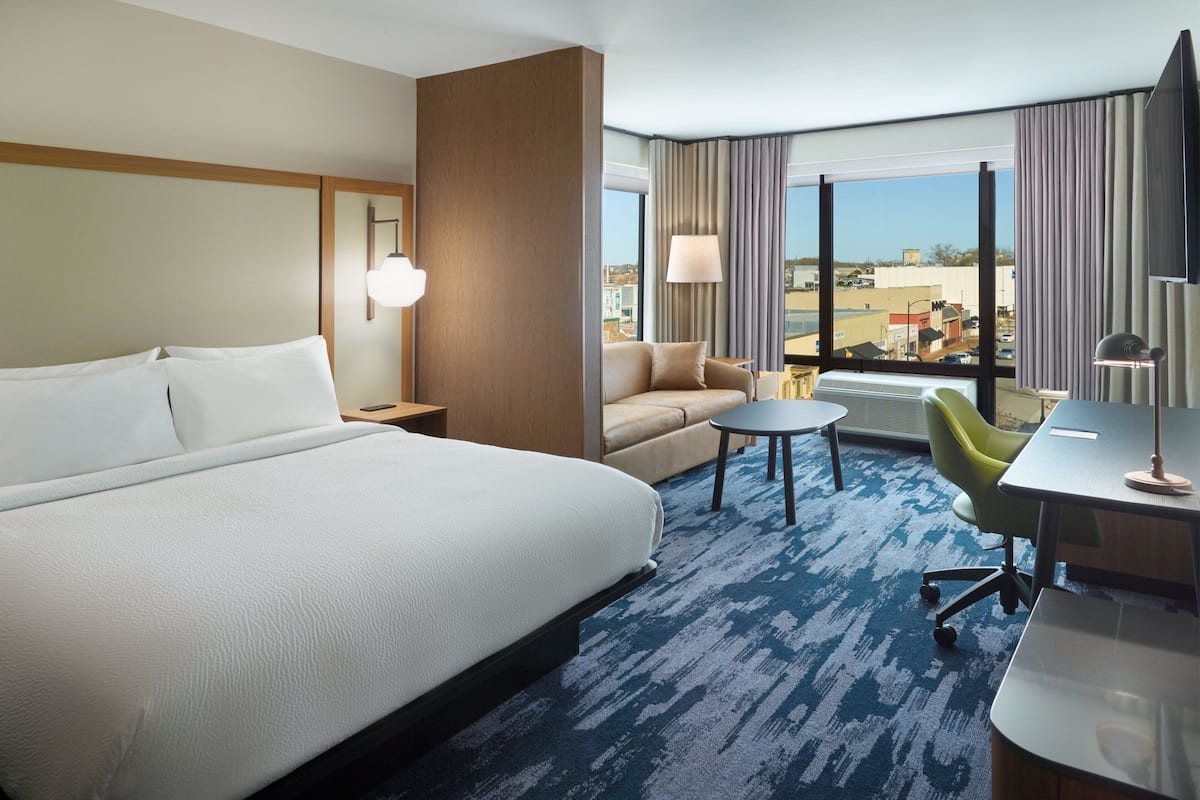 A hotel room with a large bed, a sofa, a desk, and a view of the city.