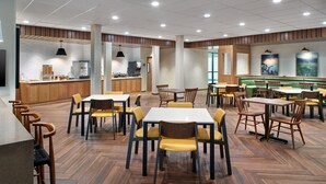 A spacious dining area with multiple tables and chairs, a kitchen in the background, and a modern design with wooden flooring and pendant lighting. - Fairfield Inn & Suites by Marriott Decatur (Decatur)