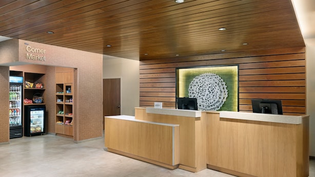A reception area with a wooden reception desk, a 'Corner Market' sign, and a wall-mounted decorative piece. - Fairfield Inn & Suites by Marriott Decatur (Decatur)