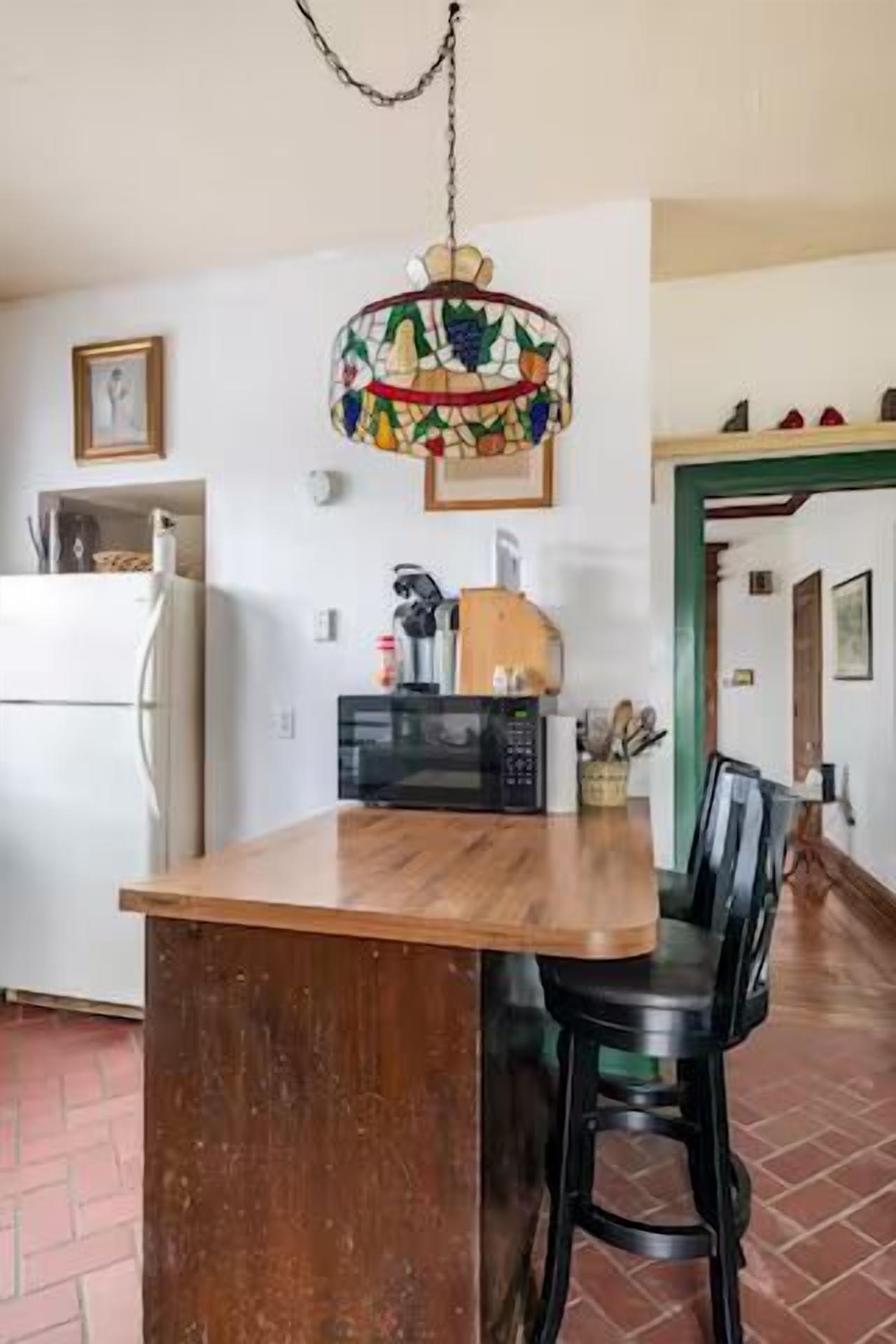 Une cuisine avec un îlot central en bois, un réfrigérateur, un four à micro-ondes et un luminaire suspendu.