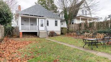 A residential house with a covered porch, a front yard with grass and fallen leaves, and a wooden fence.
