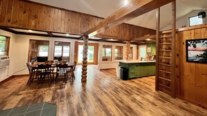 A spacious kitchen with wooden beams, a dining area with a table and chairs, and a view of the outdoors through large windows. - Charming Lakehouse private yard, boat dock/wifi. (Frankling Vermont)