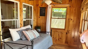 A wooden cabin bedroom with a bed, a ceiling fan, and large windows. - Charming Lakehouse private yard, boat dock/wifi. (Frankling Vermont)