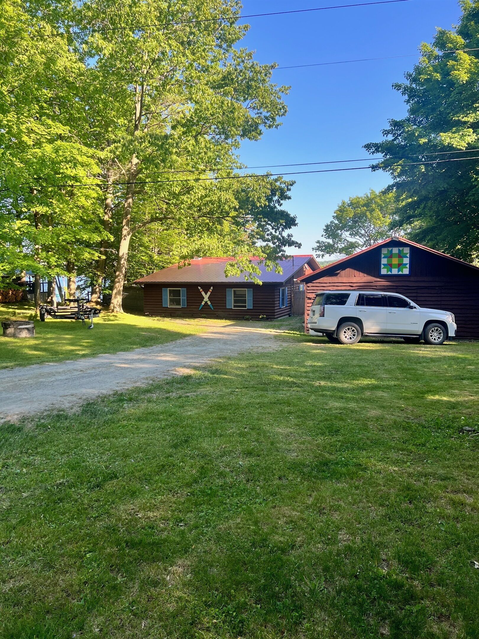 A rustic cabin with a red roof, a white SUV parked in front, and a large tree to the left.
