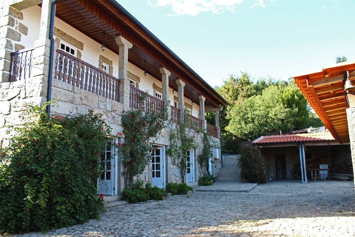 Un edificio de piedra con un balcón, un patio empedrado y una zona cubierta con techo rojo.