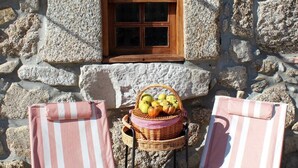 A stone building with a window, two striped beach chairs, and a wicker basket with fruits.