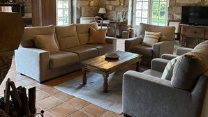 A cozy living room with a stone wall, wooden ceiling, and a fireplace. There are two sofas, a coffee table, and a TV.