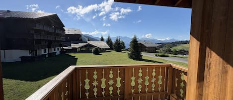A wooden balcony with a view of a building and mountains.