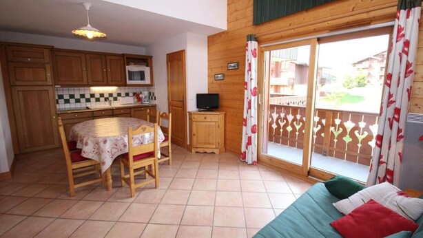 A compact kitchen with wooden cabinets, a dining table with chairs, a small TV, and a balcony with patterned curtains. - 100m from ski slopes, 1st floor, view mountain, balcony, tv, 40m², Les Saisies (Les Saisies)