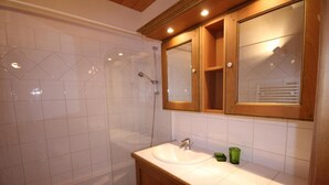 Een badkamer met een douche, wastafel en houten kasten.