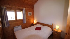 Een gezellige kamer met een houten plafond, een bed met wit beddengoed en een rode kussen, twee bedlampen en een raam met gordijnen.