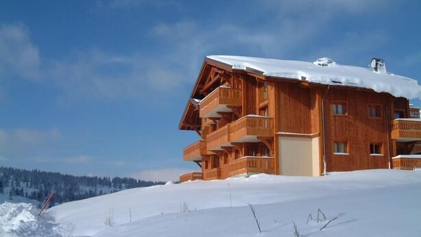 Een houten chalet met meerdere balkons, gelegen in een besneeuwd landschap.