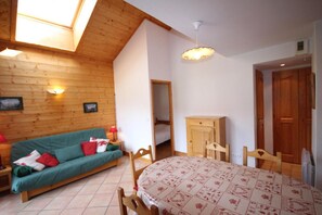 A cozy room with a wooden ceiling, a green sofa, a dining table with chairs, and a wooden cabinet.