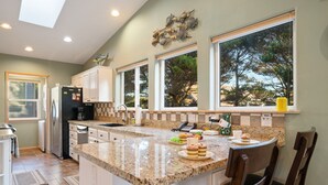 A kitchen with a large island, white cabinets, a built-in oven, and a window overlooking trees.