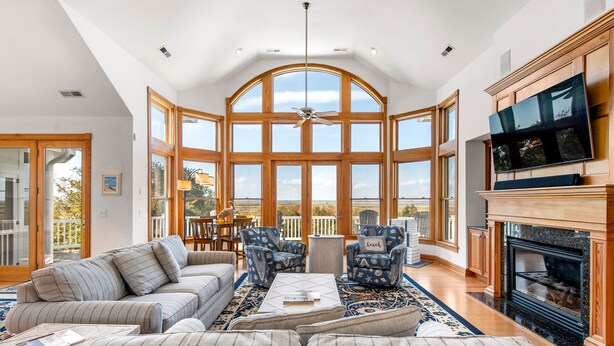 A spacious living room with a large bay window, a fireplace, and a television. - Wellfleet: Soundfront | Pool and Hot Tub | Dogs OK (Corolla)