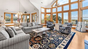 A spacious living room with large windows, a patterned rug, and a view of the outdoors. - Wellfleet: Soundfront | Pool and Hot Tub | Dogs OK (Corolla)