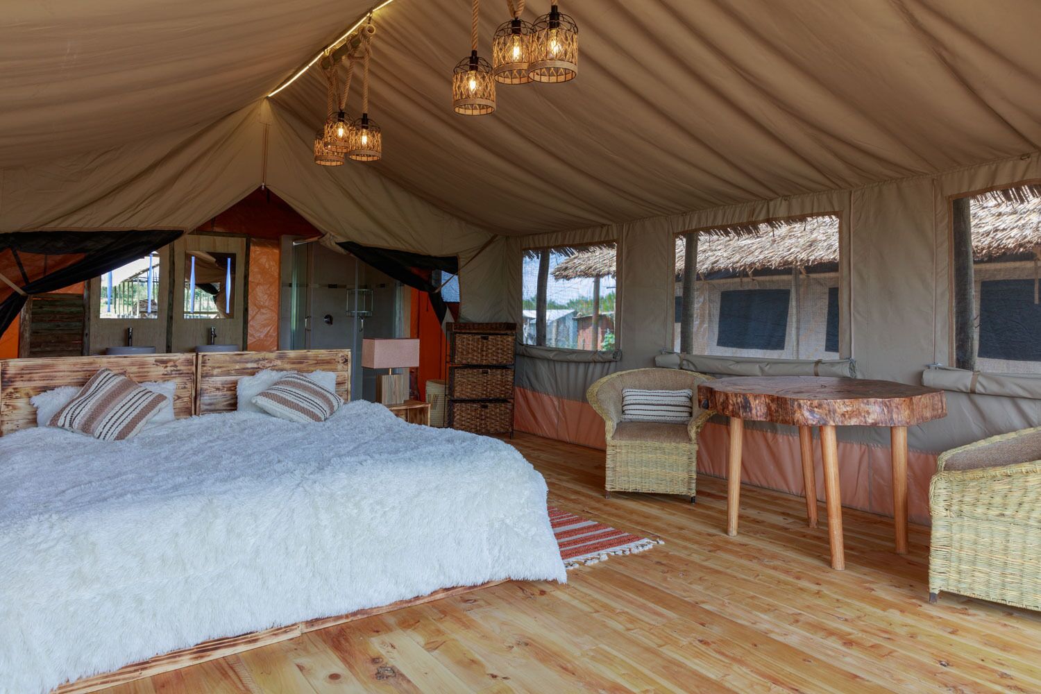 A tented accommodation with a large bed, wicker furniture, and hanging lights.