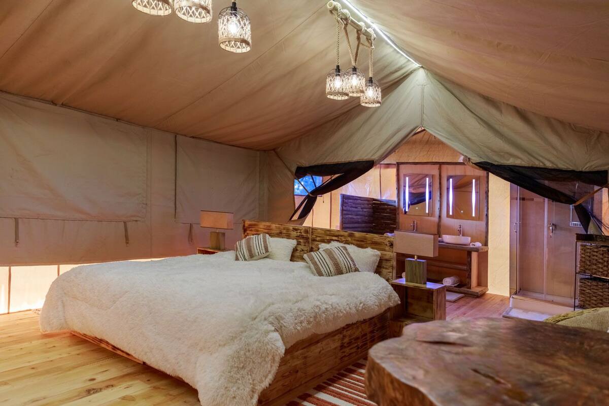 A cozy tented accommodation with a large bed, wooden headboard, and a small seating area.