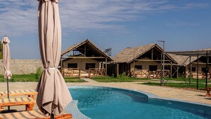 Une piscine entourée de chaises longues et de parasols, avec des huttes aux toits de chaume.