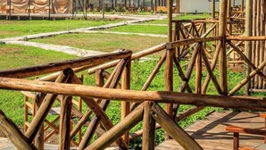 Un espace extérieur rustique agrémenté de constructions à toits de chaume, de bancs en bois et d’un ciel dégagé.