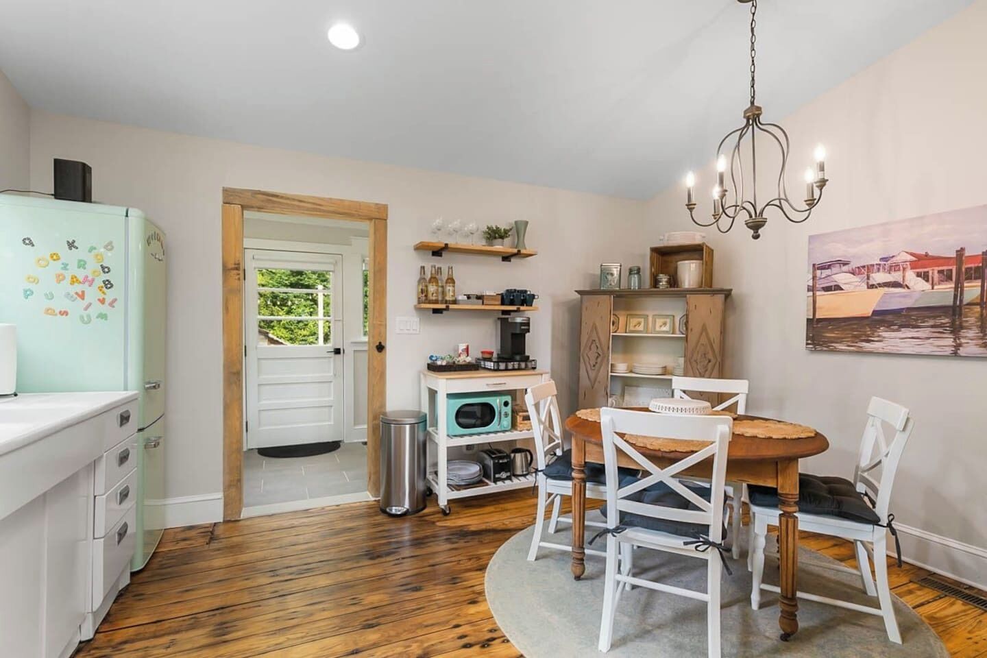 A kitchen with a refrigerator, a coffee machine, and a dining table with chairs.