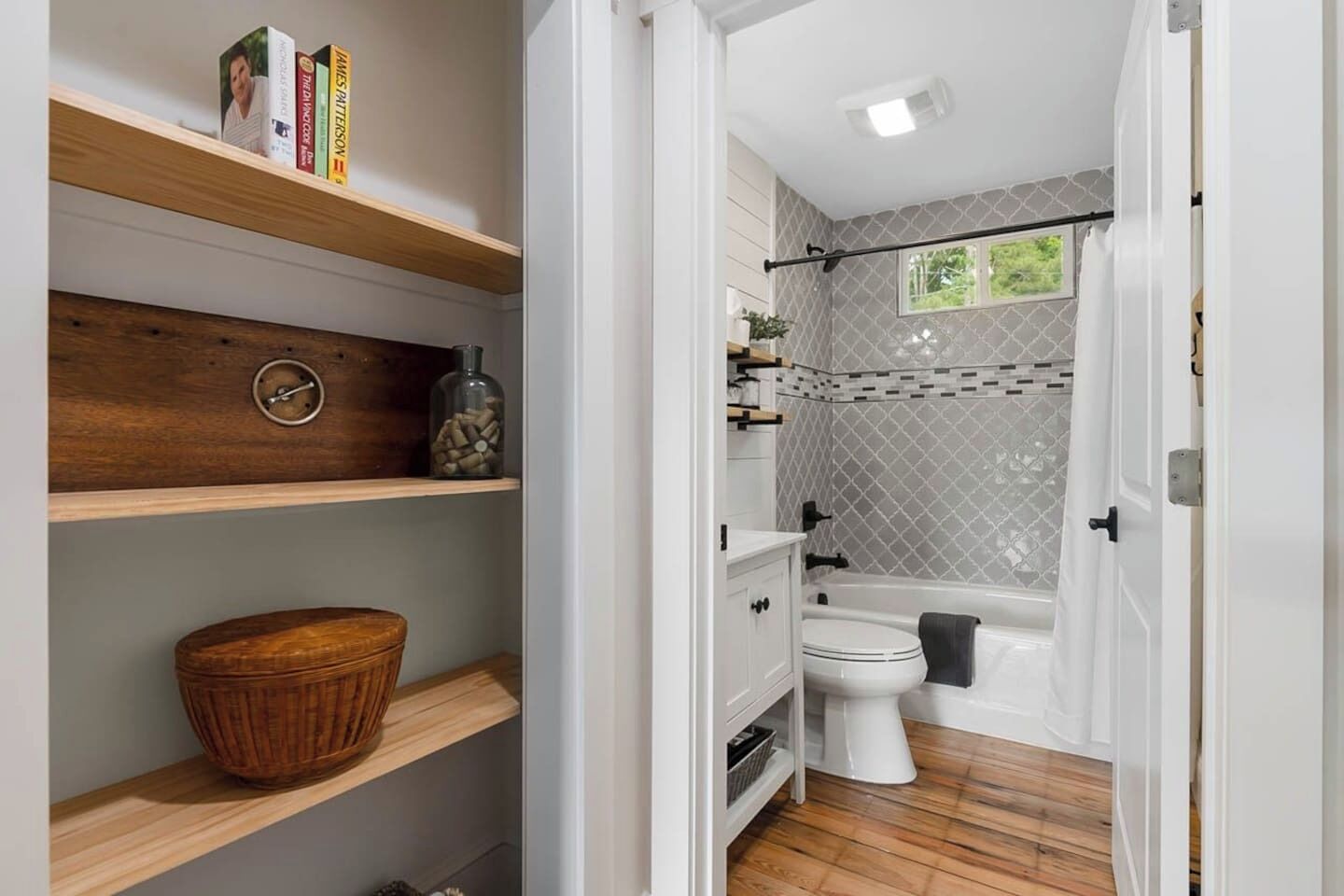Un baño con inodoro, bañera y estantes con libros y un cuenco de madera.