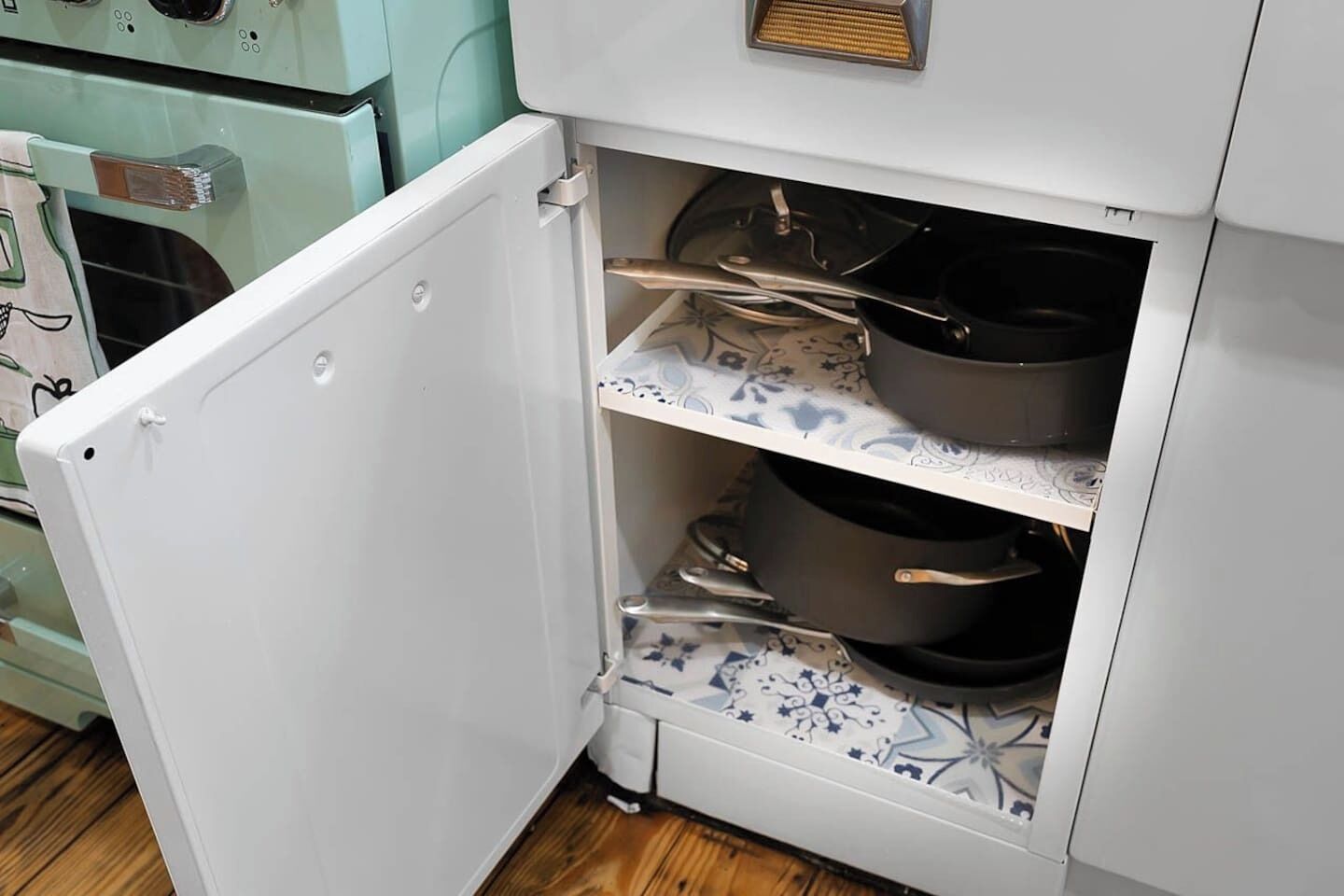 A kitchen with a white refrigerator, a stove, and a shelf with pots and pans.