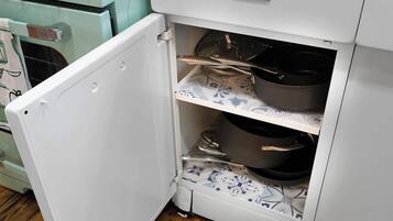 A kitchen with a white refrigerator, a stove, and a shelf with pots and pans.