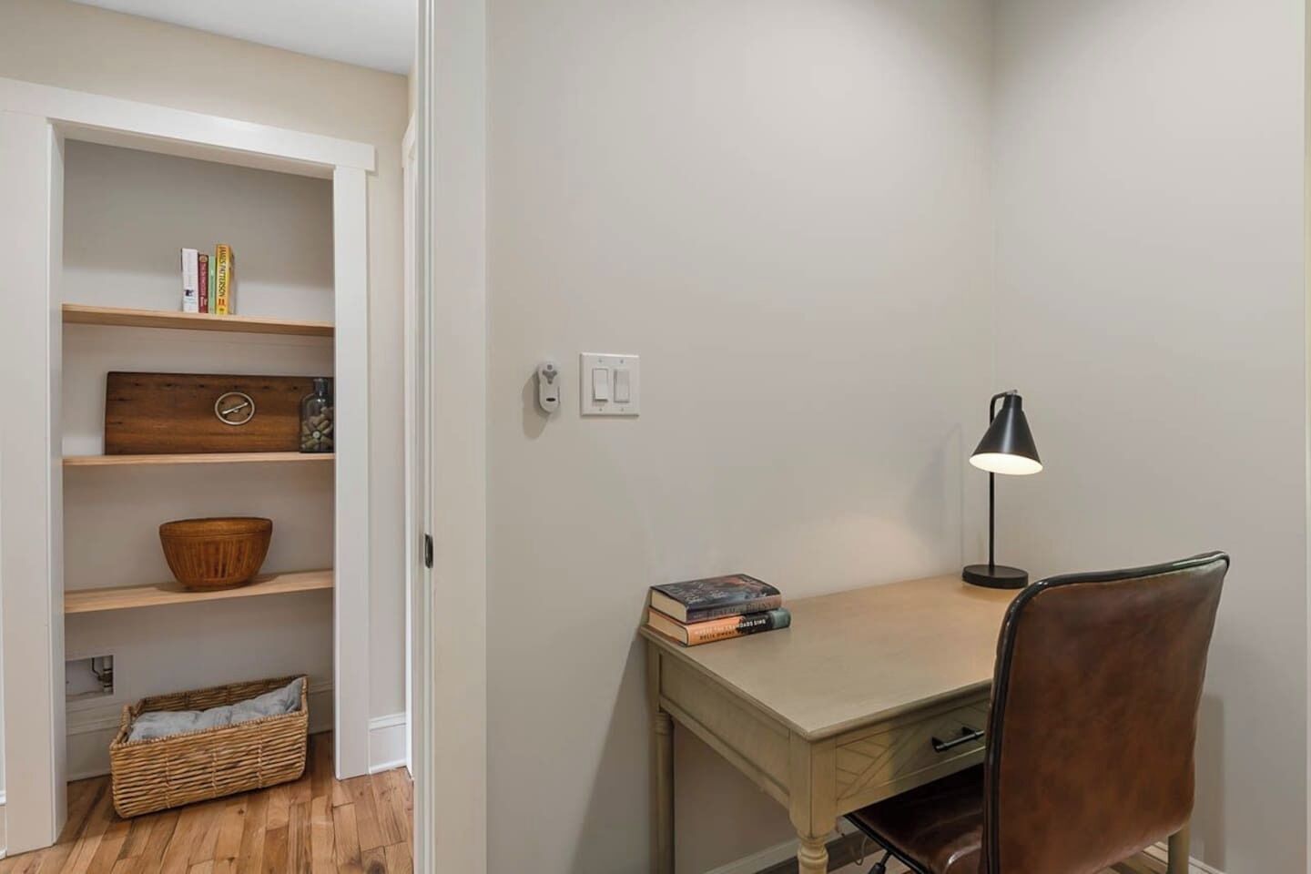 A study with a desk, chair, lamp, and shelves with books and decorative items.