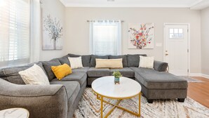 A modern living room with a grey sectional sofa, a round coffee table, and a large window with blinds. - ★ Lux Modern Retreat ★ Downtown ★ King Beds ★ (Durham)