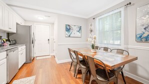 A kitchen with white cabinets, a wooden dining table with chairs, and a window with blinds. - ★ Lux Modern Retreat ★ Downtown ★ King Beds ★ (Durham)
