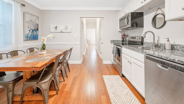 A modern kitchen with white cabinetry, stainless steel appliances, and a wooden dining table with chairs. - ★ Lux Modern Retreat ★ Downtown ★ King Beds ★ (Durham)